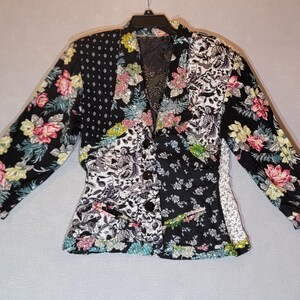May include: A long-sleeved blazer featuring a patchwork design of black fabric with floral patterns in pink, yellow, and green, alongside black and white botanical prints. The garment includes a notched lapel, three front buttons, and pockets.