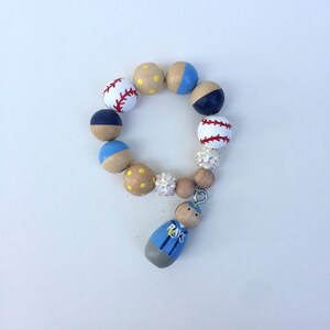 May include: A wooden bead necklace with a baseball theme. The beads are painted with baseballs, blue and yellow polka dots, and a wooden figure wearing a blue shirt with the word "RAYS" on it.