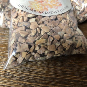 May include: A clear plastic bag filled with small, irregular-shaped brown and beige stones. The bag is labeled "LivingArrangementEtsy.com".