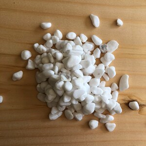May include: A pile of white, smooth, rounded river rocks on a light brown wooden surface.