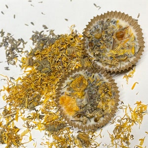 May include: Two brown paper cupcake liners filled with a white wax mixture and dried flowers. The flowers are a mix of yellow and purple.