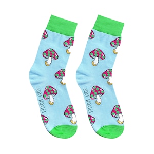 May include: A pair of light blue socks with a repeating pattern of red and green polka-dotted mushrooms. The socks have green cuffs and toes. The text "SOXI WOXIES" is printed vertically on the side of each sock.