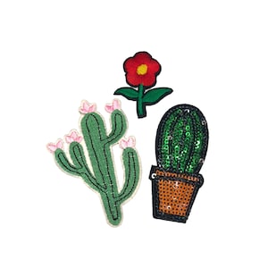 Peut inclure: Trois patchs brodés thermocollants représentant des cactus et des fleurs. Les patchs de cactus sont verts avec des fleurs roses et le patch de fleur est rouge avec des feuilles vertes.