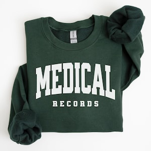 May include: A dark green sweatshirt with the words "MEDICAL RECORDS" printed in bold white letters. The sweatshirt is folded, with the sleeves rolled up, and is set against a white background.