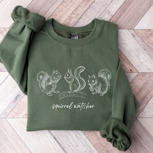 May include: A green sweatshirt with a white graphic of three squirrels and the text "squirrel watcher".