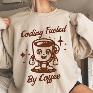 May include: A beige sweatshirt with brown text that reads "Coding Fueled by Coffee". A cartoon coffee cup with a smiling face is in the center of the text.