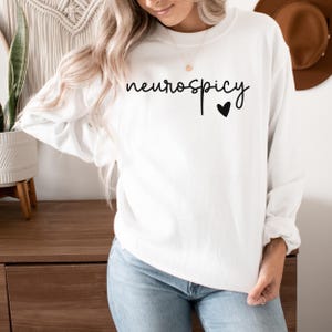 Op de afbeelding: Witte trui met de tekst "neurospicy" in zwarte cursieve letters en een klein zwart hartje.