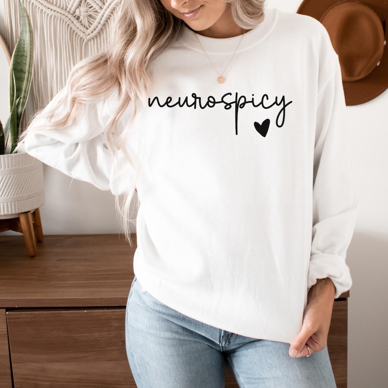 Op de afbeelding: Witte trui met de tekst "neurospicy" in zwarte cursieve letters en een klein zwart hartje.