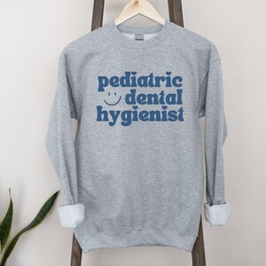 May include: Gray sweatshirt with the text "pediatric dental hygienist" in blue with a smiley face.