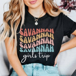 May include: Black t-shirt with a rainbow design that says "Savannah girls trip" in a retro font.
