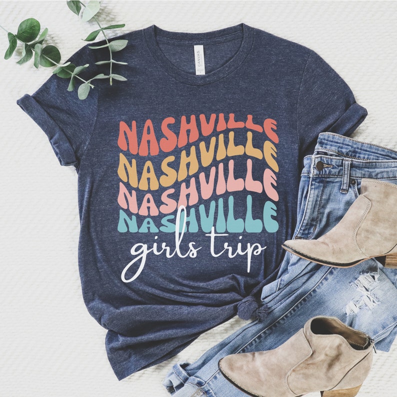 K&ouml;nnte beinhalten: Ein marineblaues T-Shirt mit dem Text "Nashville girls trip" in einem Regenbogen-Farbschema. Der Text ist &uuml;bereinander angeordnet und in einer Retro-Schriftart.
