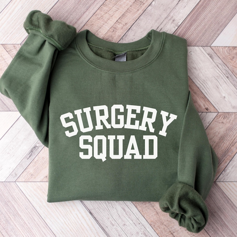May include: A green sweatshirt with the text "SURGERY SQUAD" in white letters.