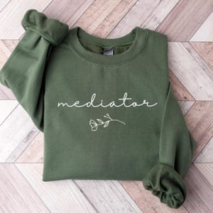 May include: A green sweatshirt with the word "mediator" printed in white on the front. A small white floral design is below the text.