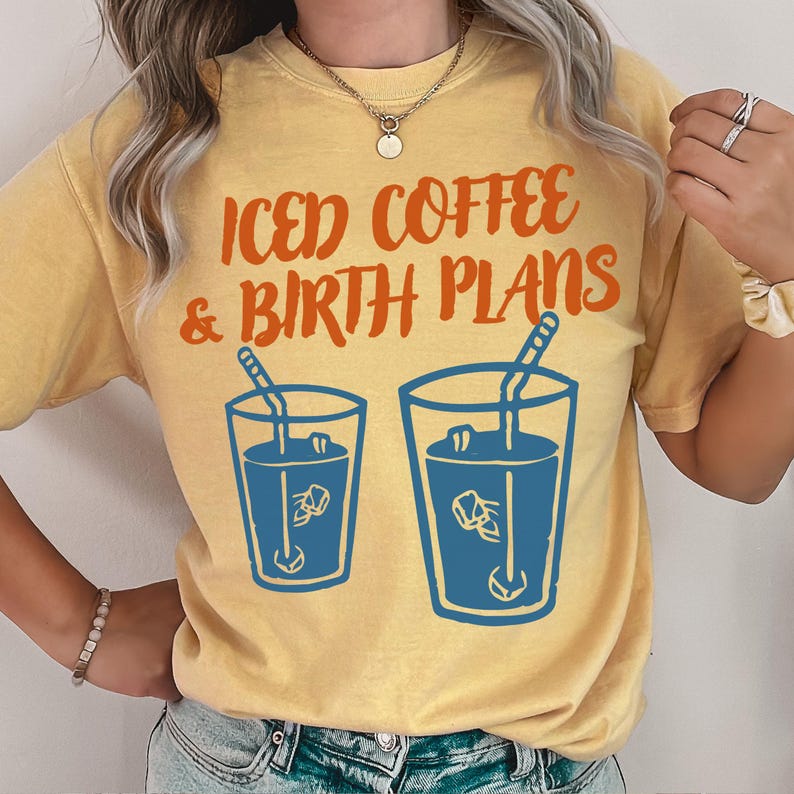 Puede incluir: Camiseta amarilla mostaza con el texto "Iced Coffee & Birth Plans" en naranja. El dise&ntilde;o incluye dos vasos azules de caf&eacute; helado con pajitas. Una camiseta informal.