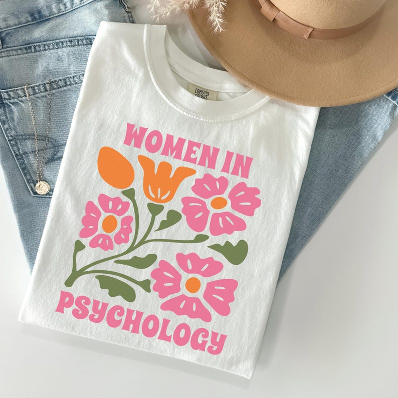 K&ouml;nnte beinhalten: Wei&szlig;es T-Shirt mit einem rosa und gr&uuml;nen Blumendesign und dem Text "Women in Psychology" in rosa.