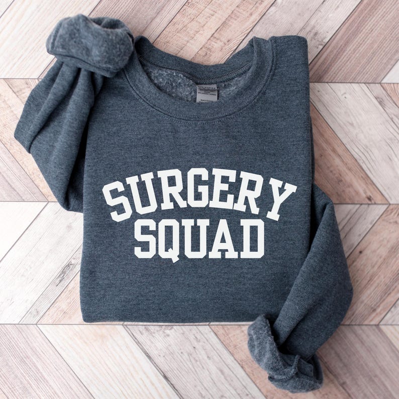 May include: A dark grey sweatshirt with the white text "SURGERY SQUAD" printed on the front.