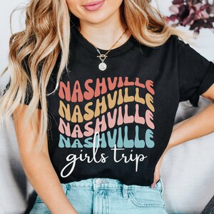 K&ouml;nnte beinhalten: Ein schwarzes T-Shirt mit einem Regenbogen-Design, auf dem in einer Retro-Schrift "Nashville girls trip" steht.