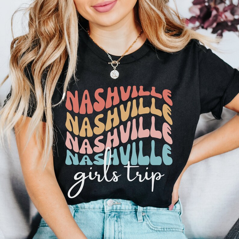 K&ouml;nnte beinhalten: Ein schwarzes T-Shirt mit einem Regenbogen-Design, auf dem in einer Retro-Schrift "Nashville girls trip" steht.