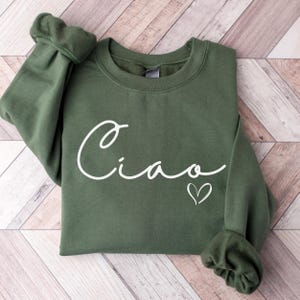 May include: A green sweatshirt with the word "Ciao" written in white cursive with a small white heart next to it.