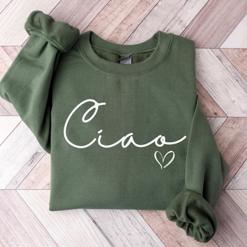 May include: A green sweatshirt with the word "Ciao" written in white cursive with a small white heart next to it.