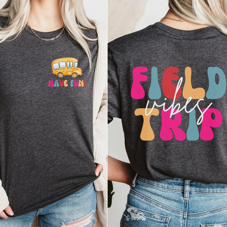 May include: A dark grey t-shirt with a yellow school bus graphic on the front and the text "HAVE FUN!" underneath. The back of the shirt has the text "FIELD vibes TRIP" in colourful, retro-style letters.