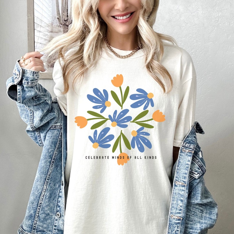 May include: White t-shirt with a blue and orange floral design and the text "Celebrate Minds of All Kinds".