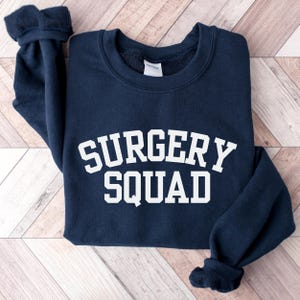 May include: A navy blue sweatshirt with the text "SURGERY SQUAD" in white.