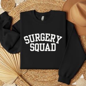 May include: Black sweatshirt with white text that reads "SURGERY SQUAD" in a collegiate-style font.