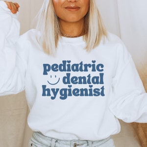 May include: White sweatshirt with blue text that reads "pediatric dental hygienist" with a smiley face.