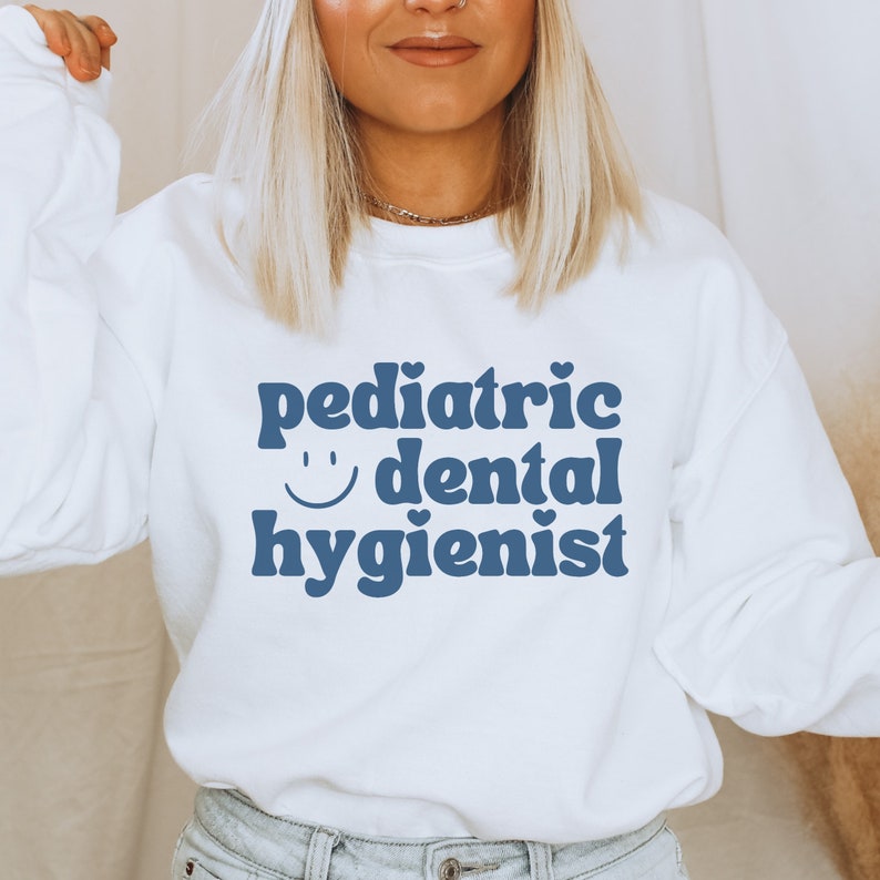 May include: White sweatshirt with blue text that reads "pediatric dental hygienist" with a smiley face.