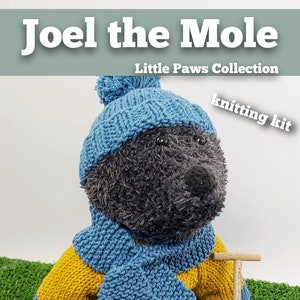 Puede incluir: Un juguete de peluche de topo con gorro, bufanda y suéter a rayas azules y amarillas. Sostiene una pala en miniatura. El texto "Joel the Mole" y "Little Paws Collection" son visibles. También se ve la frase "knitting kit".