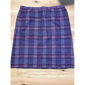 May include: A knee-length skirt featuring a plaid pattern in shades of dark navy blue, light purple, and thin magenta lines. The garment has a straight silhouette with a waistband at the top and a hemline that falls straight across the bottom edge.