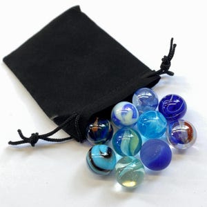 May include: A collection of ten spherical glass marbles in various shades of blue, white, and clear, featuring swirling patterns and solid colors, spilling out from a small, black, drawstring fabric pouch with black cord ties.