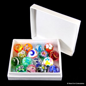 May include: A white box with a lid open, revealing a collection of 16 colorful glass marbles with intricate floral designs. The marbles are arranged in a single layer in the box.