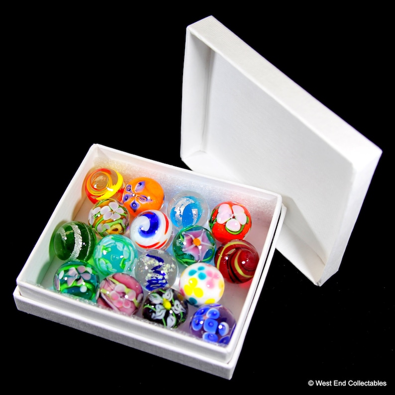 May include: A white box filled with colorful glass marbles. The marbles have various patterns and designs, including swirls, flowers, and geometric shapes.