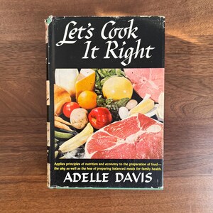 May include: A vintage cookbook titled "Let's Cook It Right" by Adelle Davis. The cover features a colorful illustration of various foods, including fruits, vegetables, and meat. The book's title is in a stylized font, and the cover is set against a dark background.