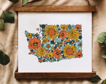 May include: A framed print of the state of Washington, outlined in a floral design. The design features a variety of flowers in shades of yellow, orange, red, and blue, including sunflowers, poppies, and daisies.