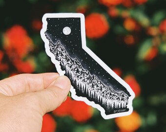 May include: Black and white sticker of the state of California with a mountain range and a crescent moon in the night sky. The sticker says "Art by Kaori" at the bottom.