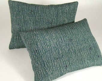 May include: Two rectangular throw pillows. The pillows are a deep teal color with a pattern of vertical white dashes. Small black accents are scattered across the surface. The pillows are arranged with one slightly behind the other.