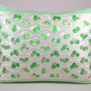 May include: A white pillow with a green and silver pattern of small circles. The pillow has a green border.
