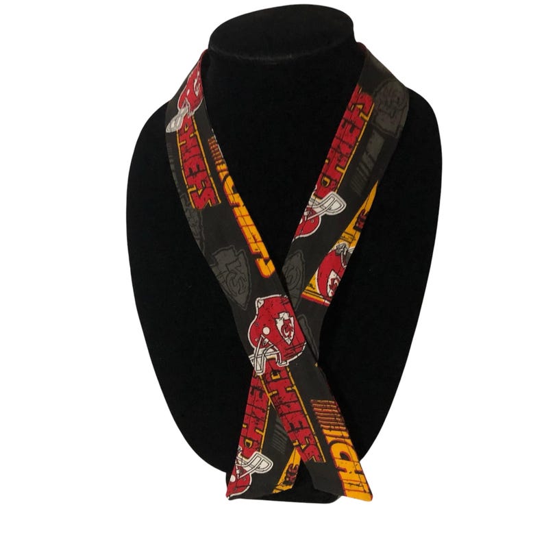 May include: A black and red lanyard with the word "Chiefs" repeated on it. The lanyard is made of fabric and has a yellow and red pattern.