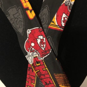 May include: Black fabric with a red, white, and yellow pattern of football helmets and the letters "KC".