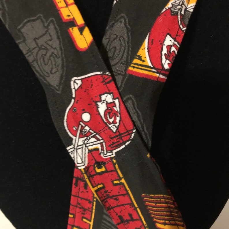 May include: Black fabric with a red, white, and yellow pattern of football helmets and the letters "KC".