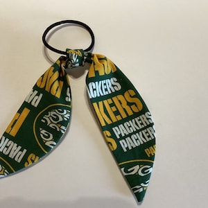 May include: Green and gold fabric hair tie with the words "Packers" repeated on it.