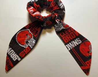 May include: A brown and orange scrunchie with a Cleveland Browns logo and the words "CLEVELAND BROWNS" printed on it.