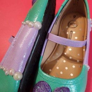 May include: A pair of green, purple, and white girls' shoes with a pearl trim and glitter bows. The shoes are size 9 and are made by Wonder Nation.