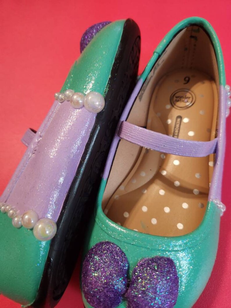 May include: A pair of green, purple, and white girls' shoes with a pearl trim and glitter bows. The shoes are size 9 and are made by Wonder Nation.