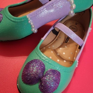 May include: A pair of green and purple glitter shoes with a pearl trim. The shoes are size 9.