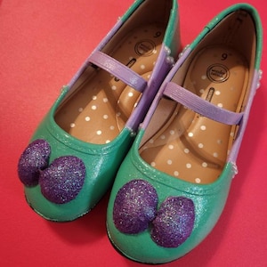May include: A pair of green and purple glitter shoes with a bow on the toe. The shoes are size 9 and have a white polka dot pattern on the inside.