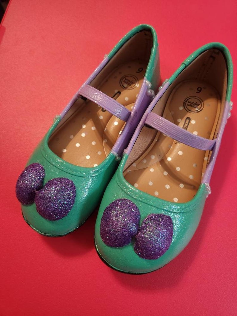 May include: A pair of green and purple glitter shoes with a bow on the toe. The shoes are size 9 and have a white polka dot pattern on the inside.